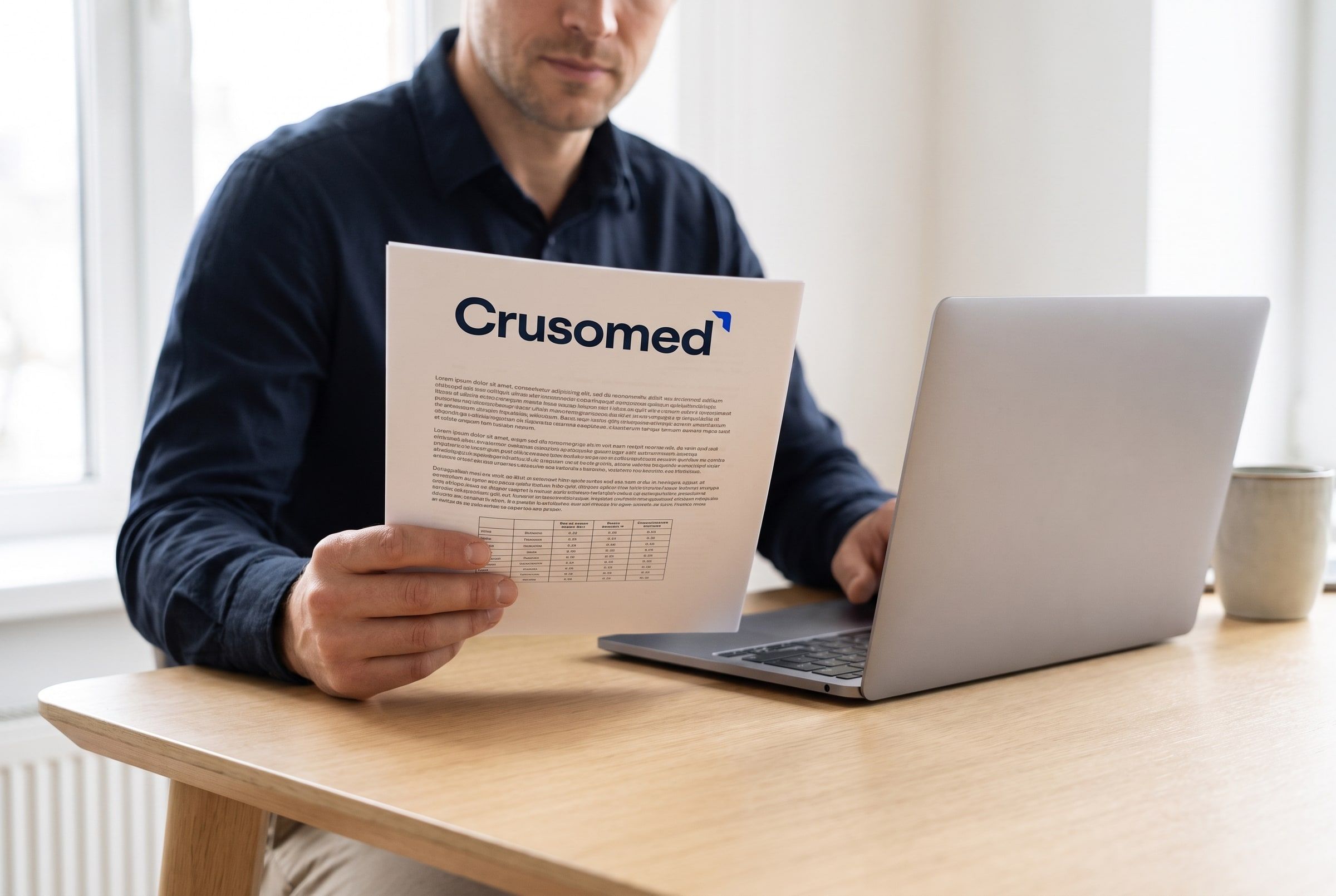 A professional at a desk in morning light reading a printed Crusomed document beside a laptop.